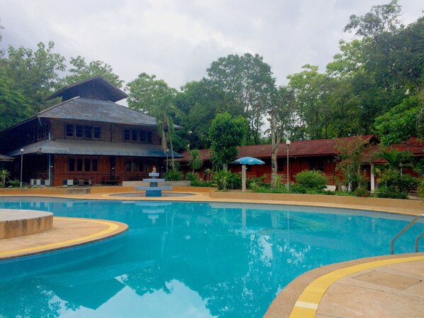 A swimming pool with a fountain, surrounded by lush greenery and traditional wooden buildings.