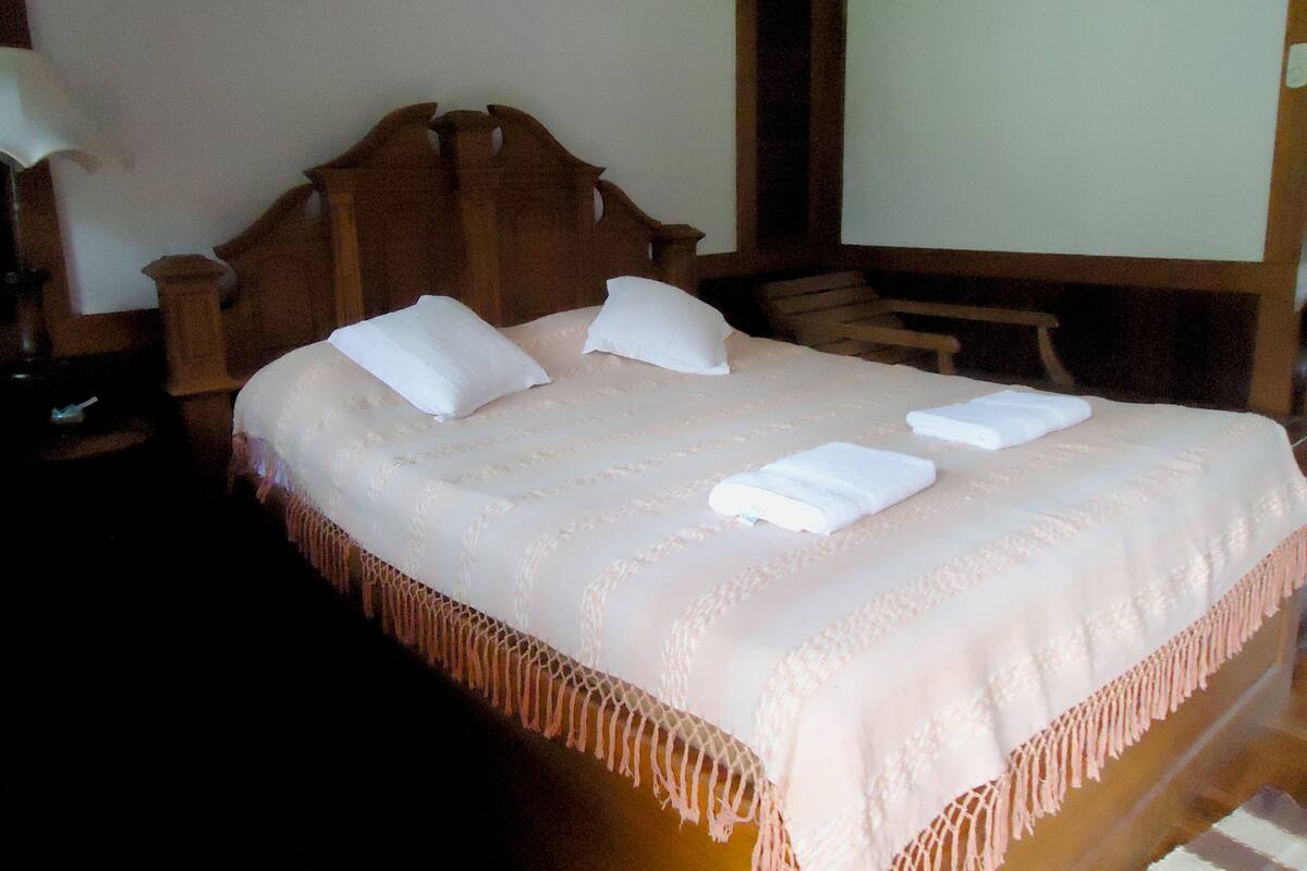A neatly made bed with pillows and folded towels, a wooden headboard, and a nightstand with a lamp.