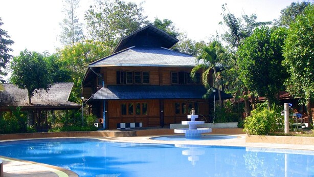 A swimming pool with a fountain, surrounded by lush greenery and a wooden building with a tiled roof. - Saksuay Klangdoi Resort (Mae Hong Son)