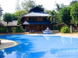 A swimming pool with a fountain, surrounded by lush greenery and a wooden building with a tiled roof. - Saksuay Klangdoi Resort (Mae Hong Son)