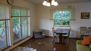 A living room with a dining table, chairs, a green sofa, a fireplace, and large windows with blinds. - Tocotoco House (Nakafurano)