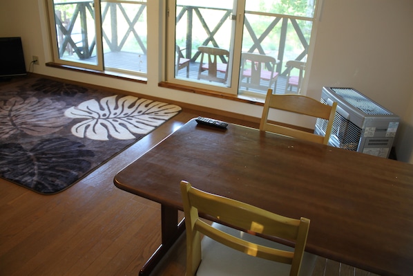 A dining area with a wooden table, chairs, a remote control, and a large window with a view of outdoor furniture. - Tocotoco House (Nakafurano)