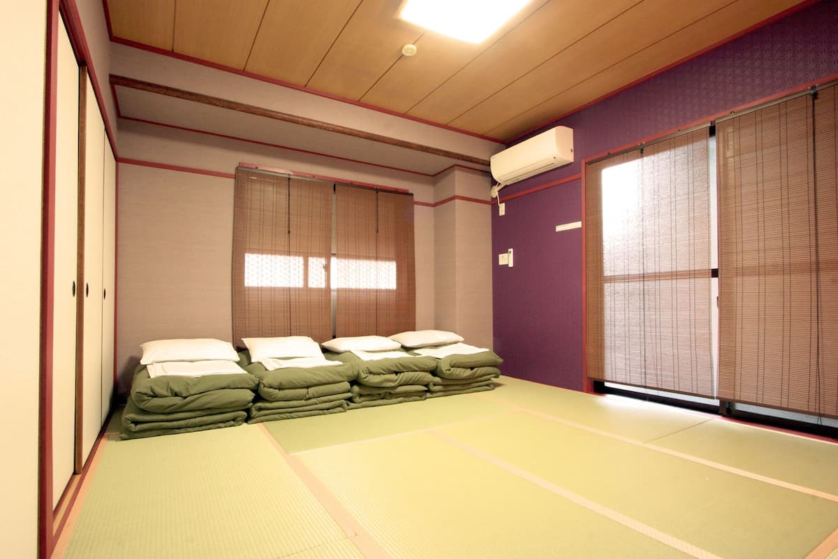 A traditional Japanese room with tatami mats, a bed with green bedding, sliding doors, and an air conditioning unit.