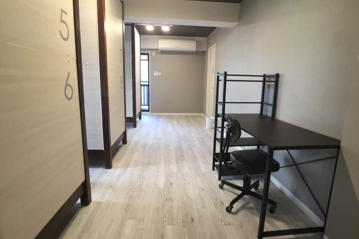 A hallway with numbered doors, a desk with a chair, and an air conditioning unit on the wall.