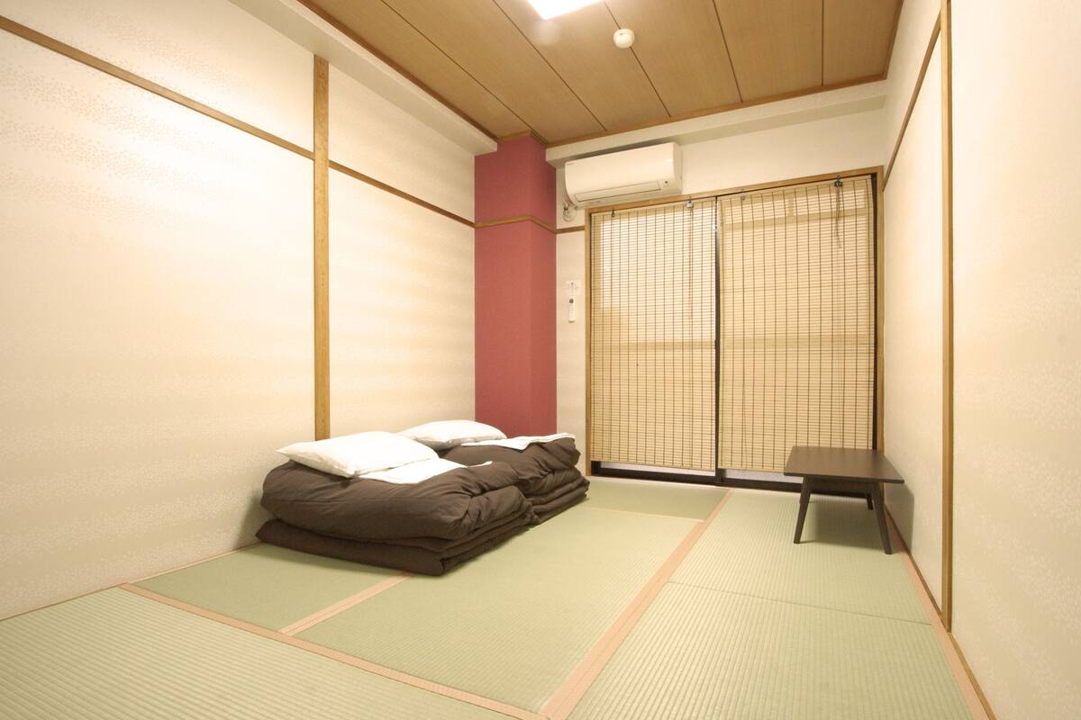 A traditional Japanese room with tatami flooring, a futon bed, a small table, and a sliding shoji screen.