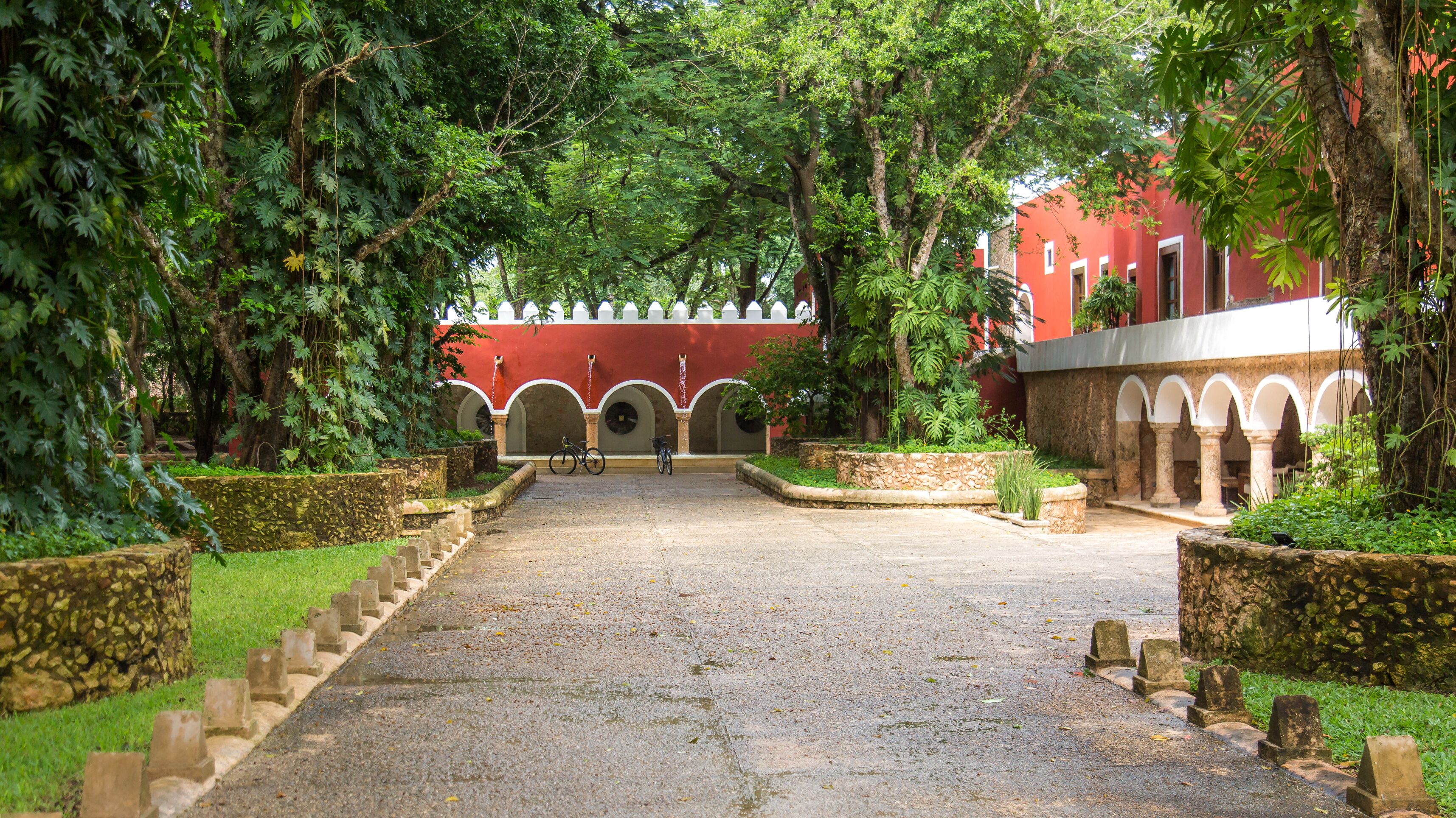 A courtyard with a paved walkway leading to a red building with arches.