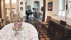A dining area with a checkered floor, a round table with a lace tablecloth, and a cabinet with glassware. - La Perla Hotel Boutique B&B (Guadalajara)