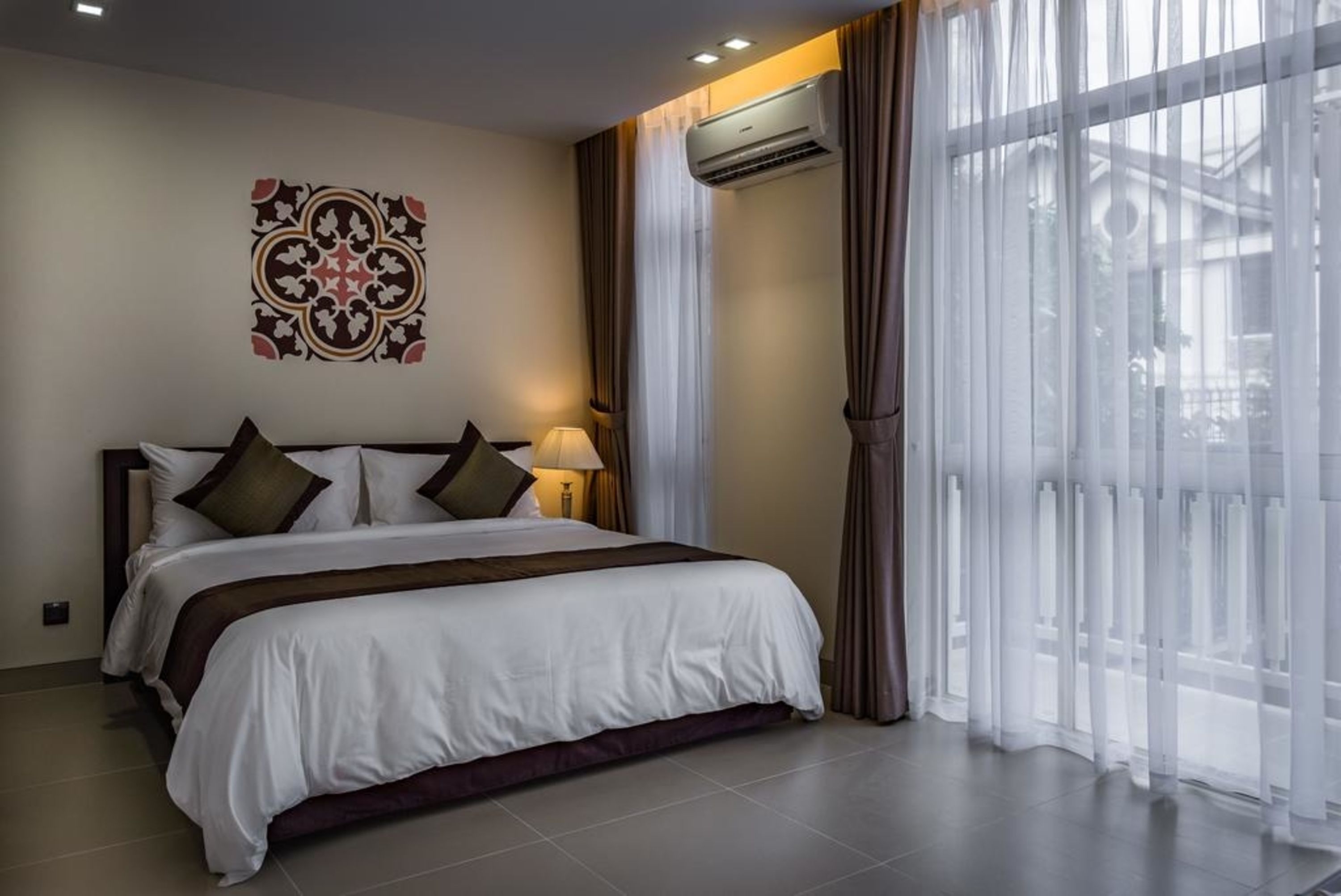 Una habitación de hotel con una cama grande, aire acondicionado de pared y cortinas traslúcidas.