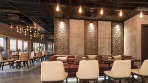 A restaurant with a modern interior, featuring a central seating area with sofas and chairs, and a bar area with tables and chairs. - Glenwood City Resort (Ho Chi Minh City)