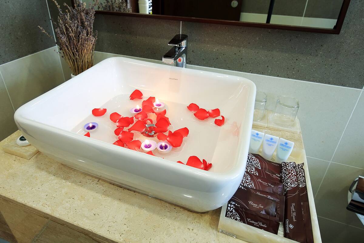 A bathroom with a white bathtub, rose petals, candles, and toiletries.