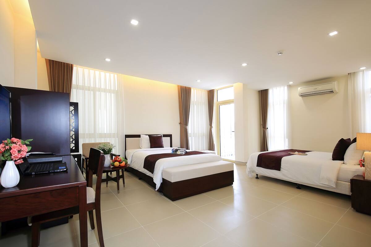 A hotel room with two beds, a desk with a laptop, a TV, and a dining area with a chair and table.