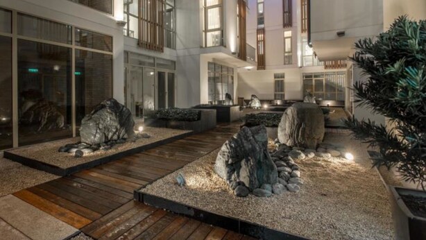 A modern building with a courtyard featuring wooden decking, large rocks, and a small water feature. - Glenwood City Resort (Ho Chi Minh City)