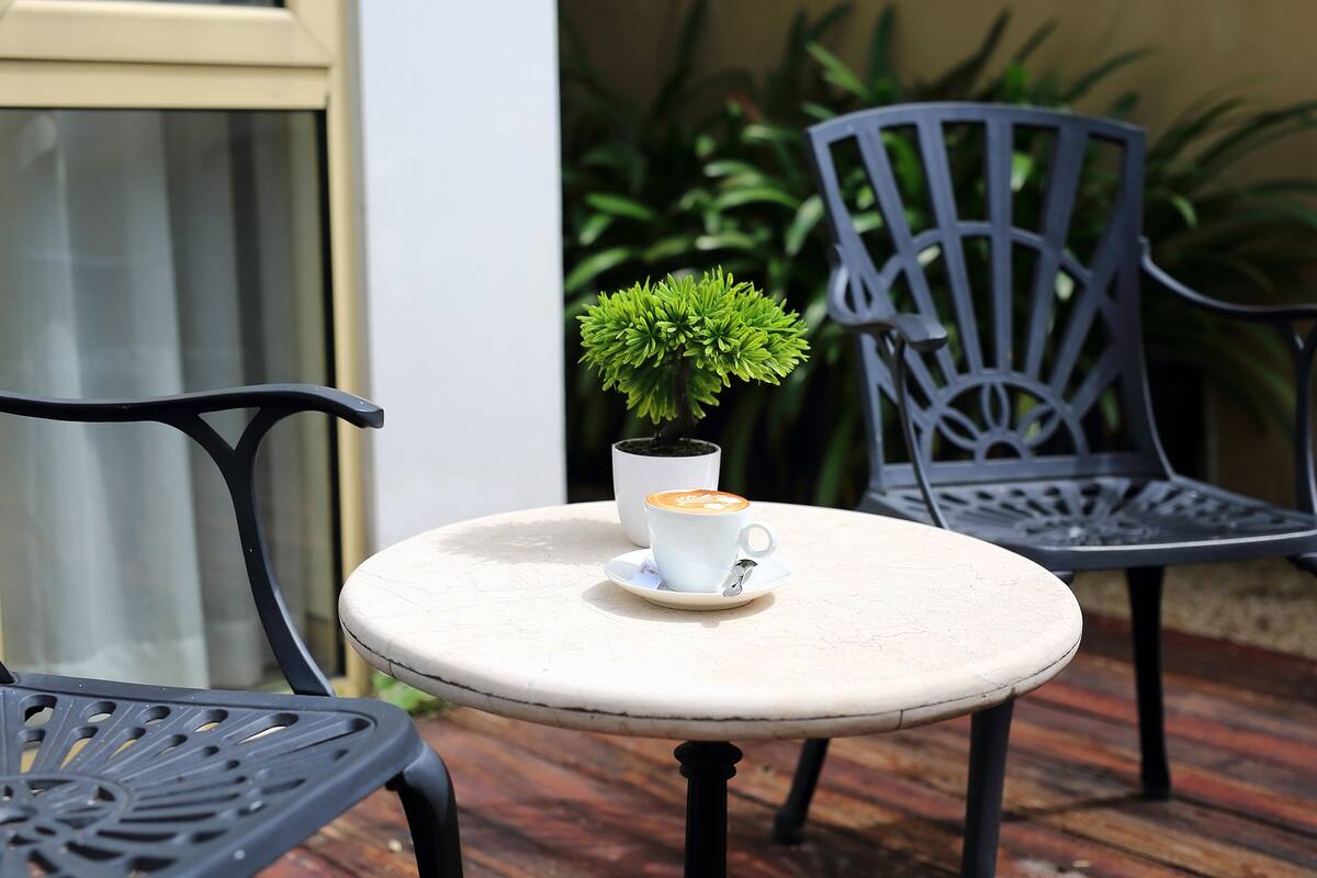A small round table with a white cup and saucer, a potted plant, and two black chairs.