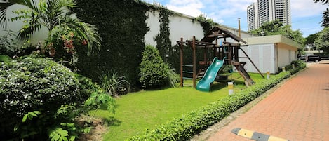 Un parque infantil con tobogán y estructura para escalar, rodeado de vegetación y un sendero pavimentado.