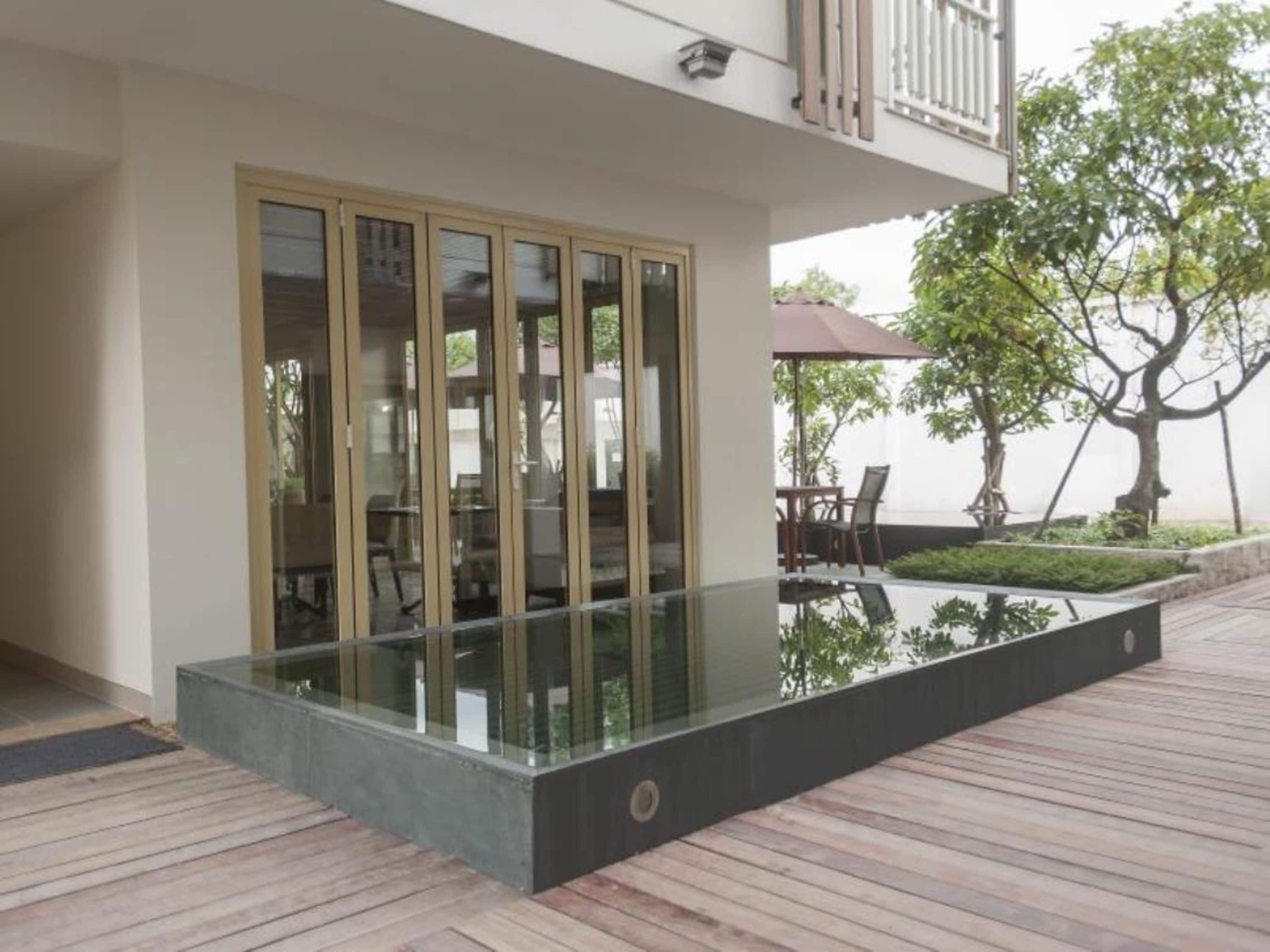 A modern outdoor area with a glass enclosure, a wooden deck, and a dining setup with chairs and an umbrella.