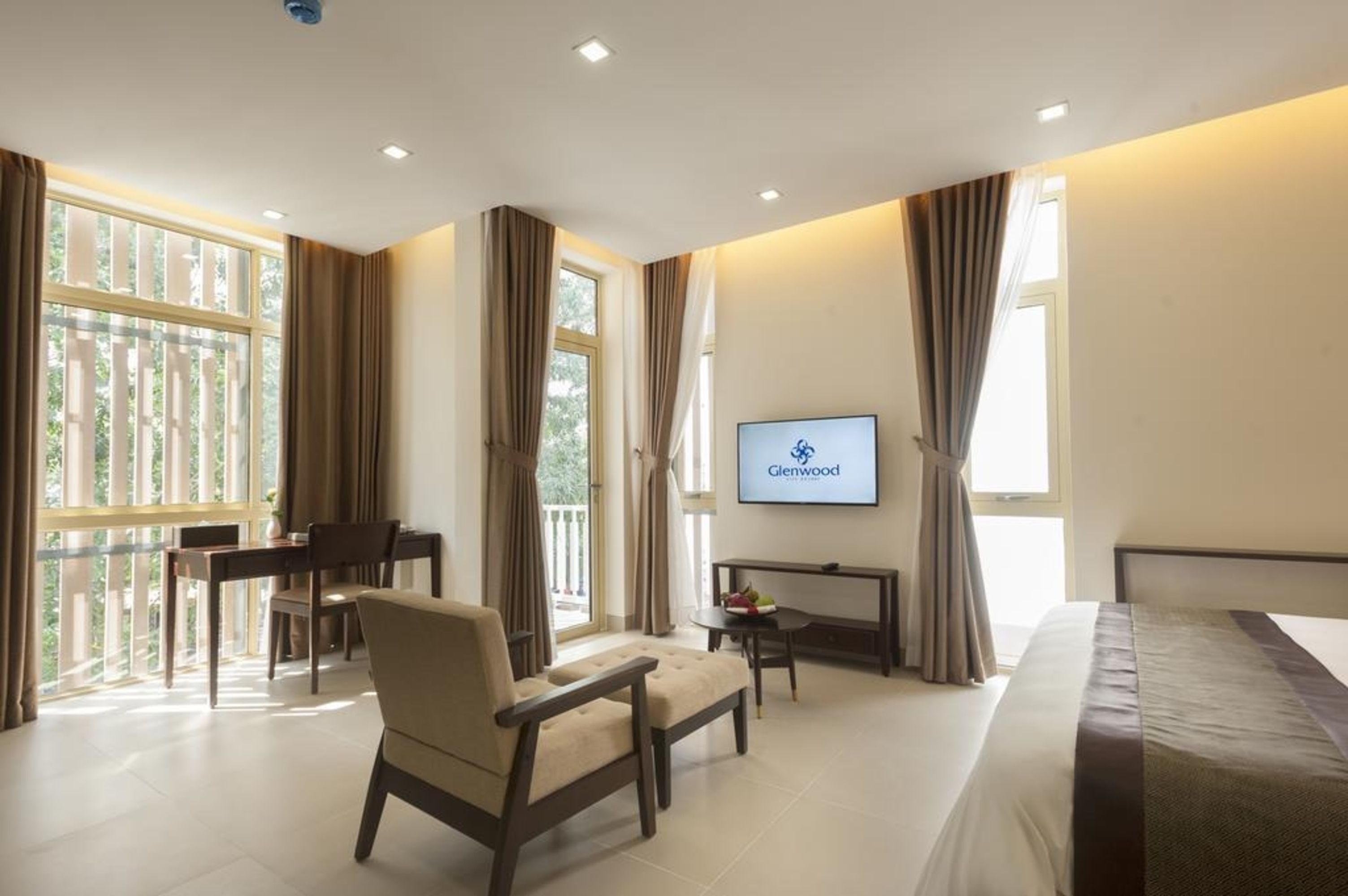 A hotel room with a bed, a desk, a chair, a TV, and large windows with curtains.