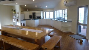 A modern kitchen with white cabinets, a central island, and a dining area with wooden benches. - Cottages on St Andrews (Havelock North)