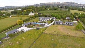 A large estate with multiple buildings, a swimming pool, and a fenced area with sheep. - Cottages on St Andrews (Havelock North)
