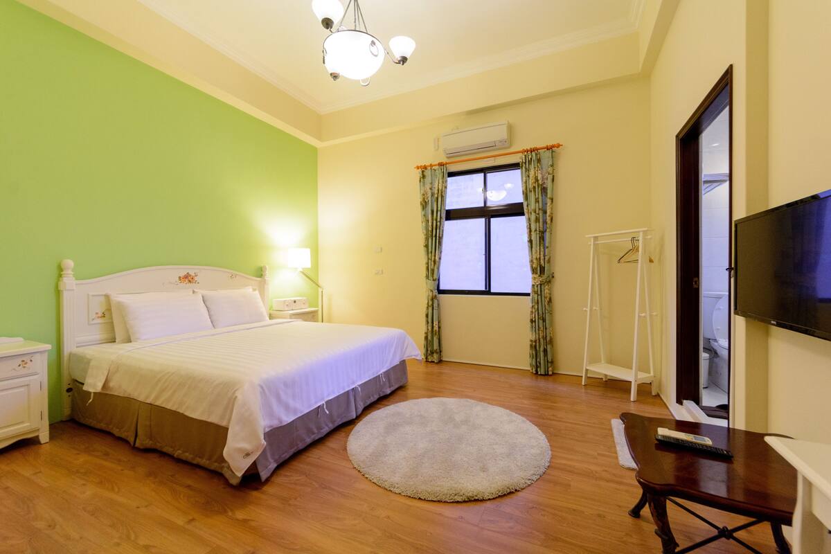 A bedroom with a bed, bedside table, lamp, round rug, and a TV on a stand.