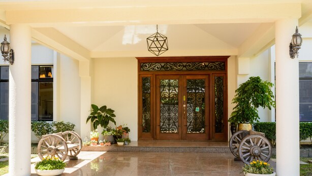 A building entrance with a large wooden door, two potted plants, and decorative wheels. - Warmhouse (Taitung)