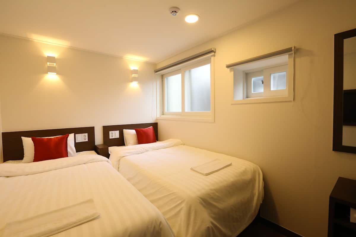 A hotel room with two beds, a window, and a wall-mounted TV.