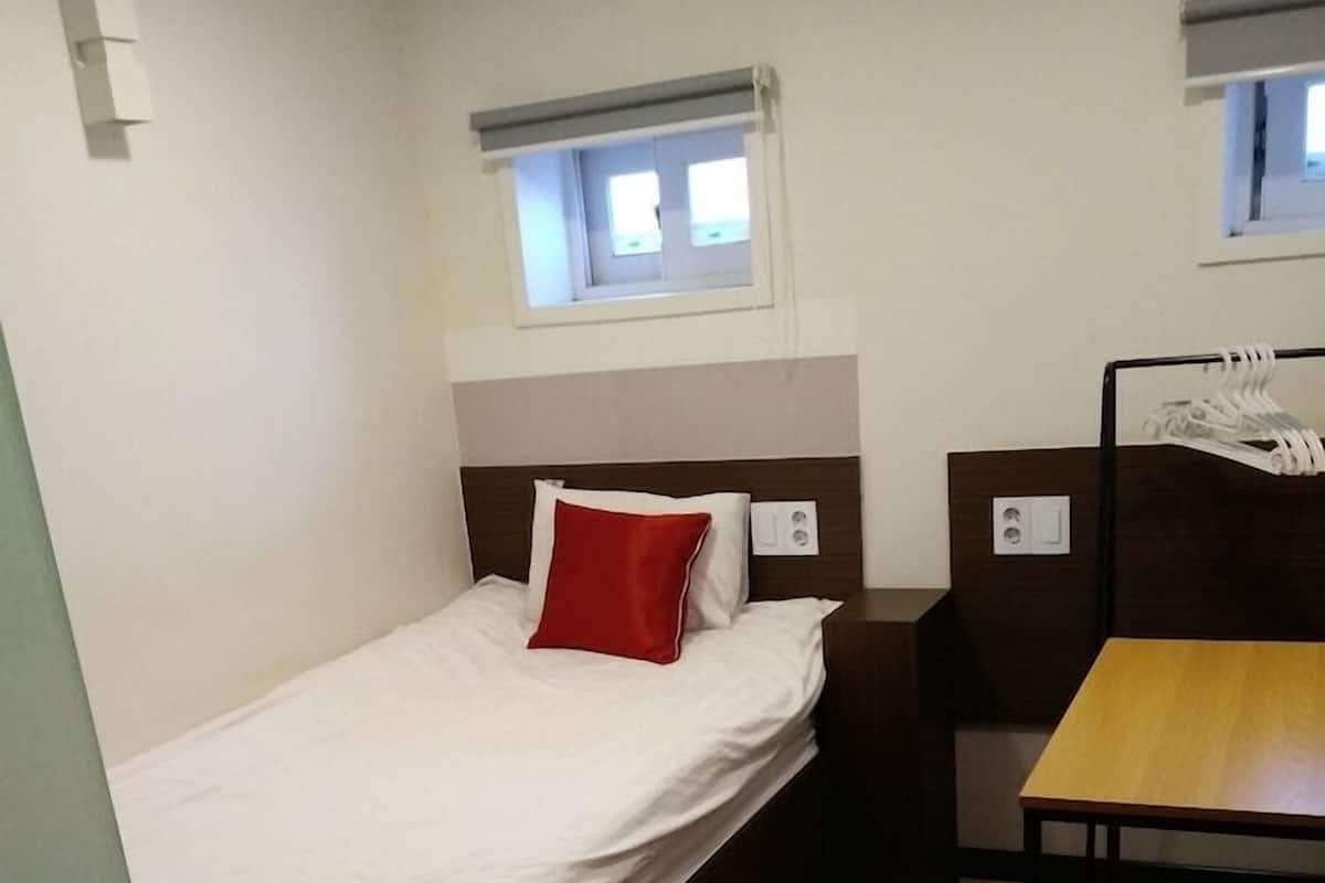 A compact room with a single bed, a small table, a chair, and a window.