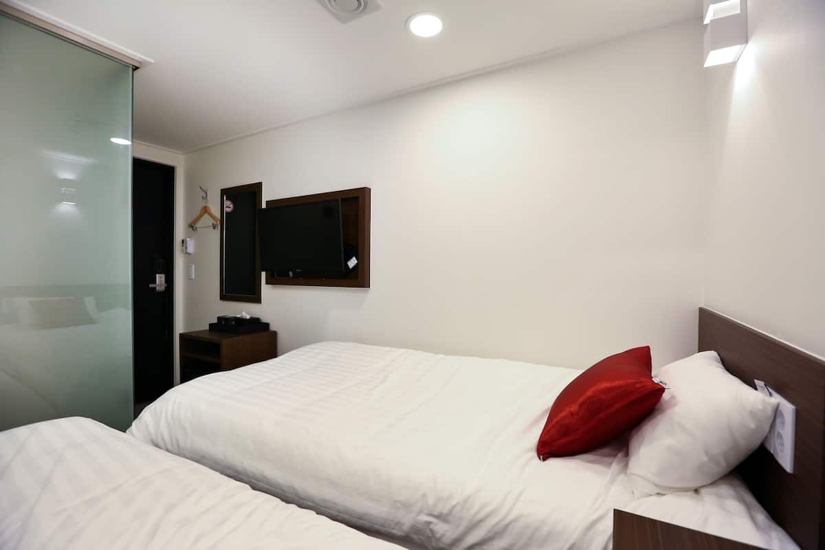A hotel room with two beds, a wooden headboard, a bedside table, a mirror, and a wardrobe.