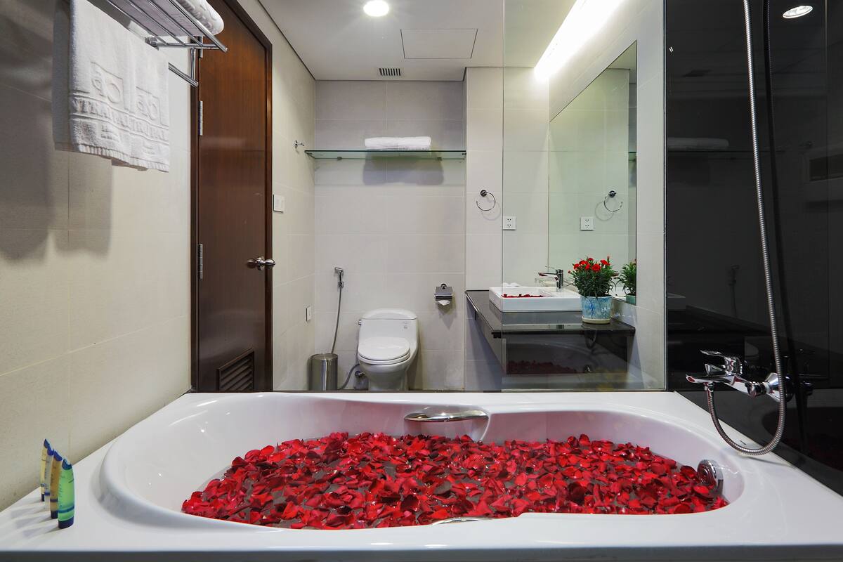 Een badkamer met een bad vol rozenblaadjes, een toilet, een wastafel en een douche.