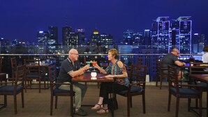 Een restaurant met houten tafels en stoelen, en een stadsachtergrond, met enkele gasten aan het dineren.