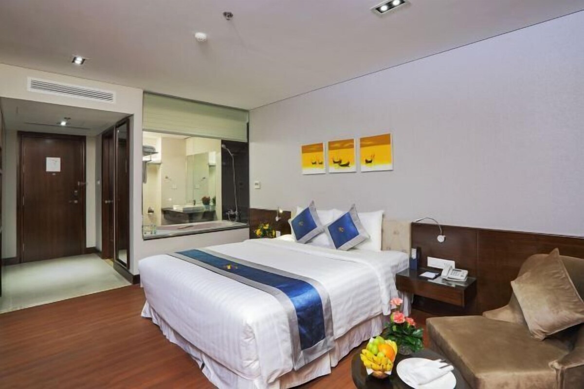 A hotel room with a large bed, a bedside table, a nightstand, a mirror, and a small seating area with a couch.