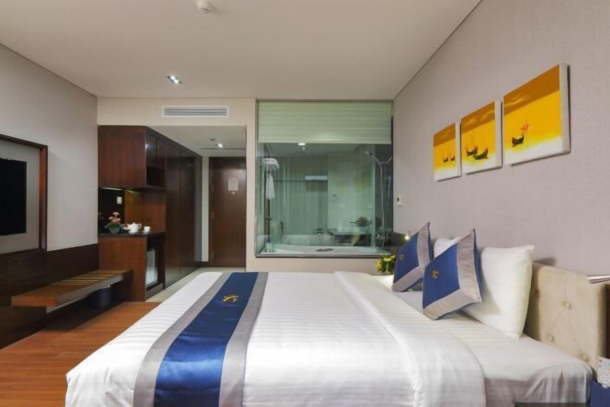A hotel room with a bed, a TV, a desk, a bathroom, and artwork on the wall.