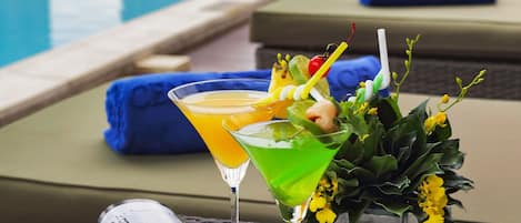 A poolside setting with a lounge chair, a drink with a garnish, and a magazine.