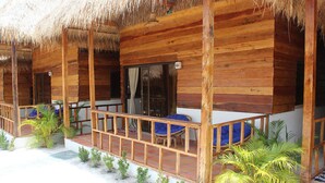 Une cabane en bois avec un toit de chaume, une véranda couverte avec des sièges et de petites plantes.