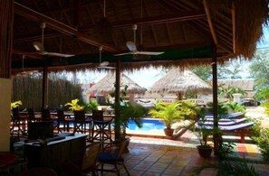 An outdoor area with a pool, lounge chairs, and thatched-roof structures. - Otres Lodge (Sihanoukville)