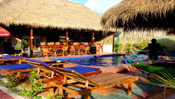 Un espace aménagé au bord de la piscine, avec des chaises longues en bois et une structure recouverte d’un toit de chaume.