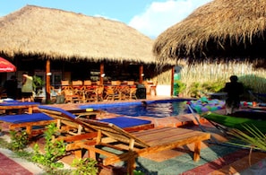 A poolside area with wooden lounge chairs and a thatched-roof structure.