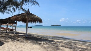 Une plage avec des parasols en chaume et des chaises longues.