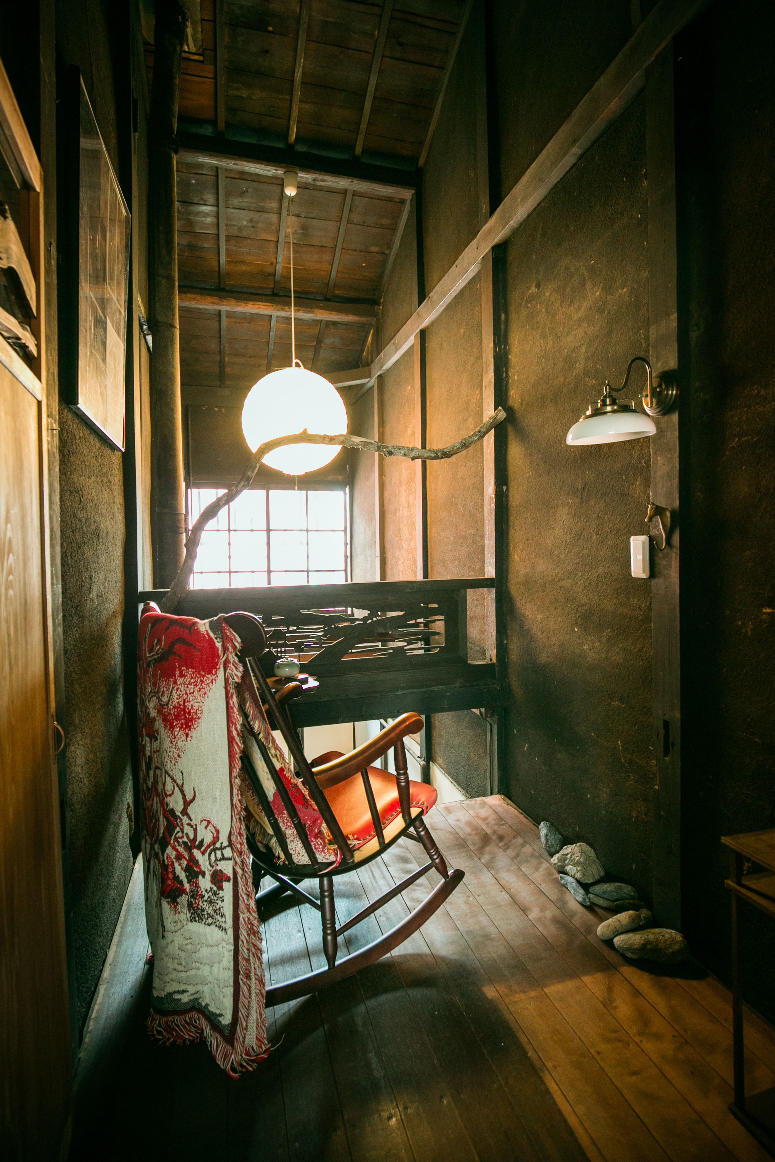 A rustic room with wooden floors, a rocking chair, a hanging light fixture, and a window with natural light.