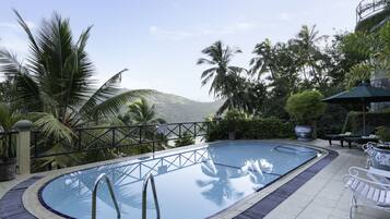 A swimming pool with a view of mountains, surrounded by palm trees and a gazebo.