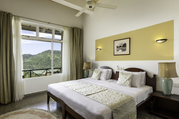 Habitación de hotel con una cama grande, vistas a un paisaje verde, un ventilador de techo y un cuadro en la pared.