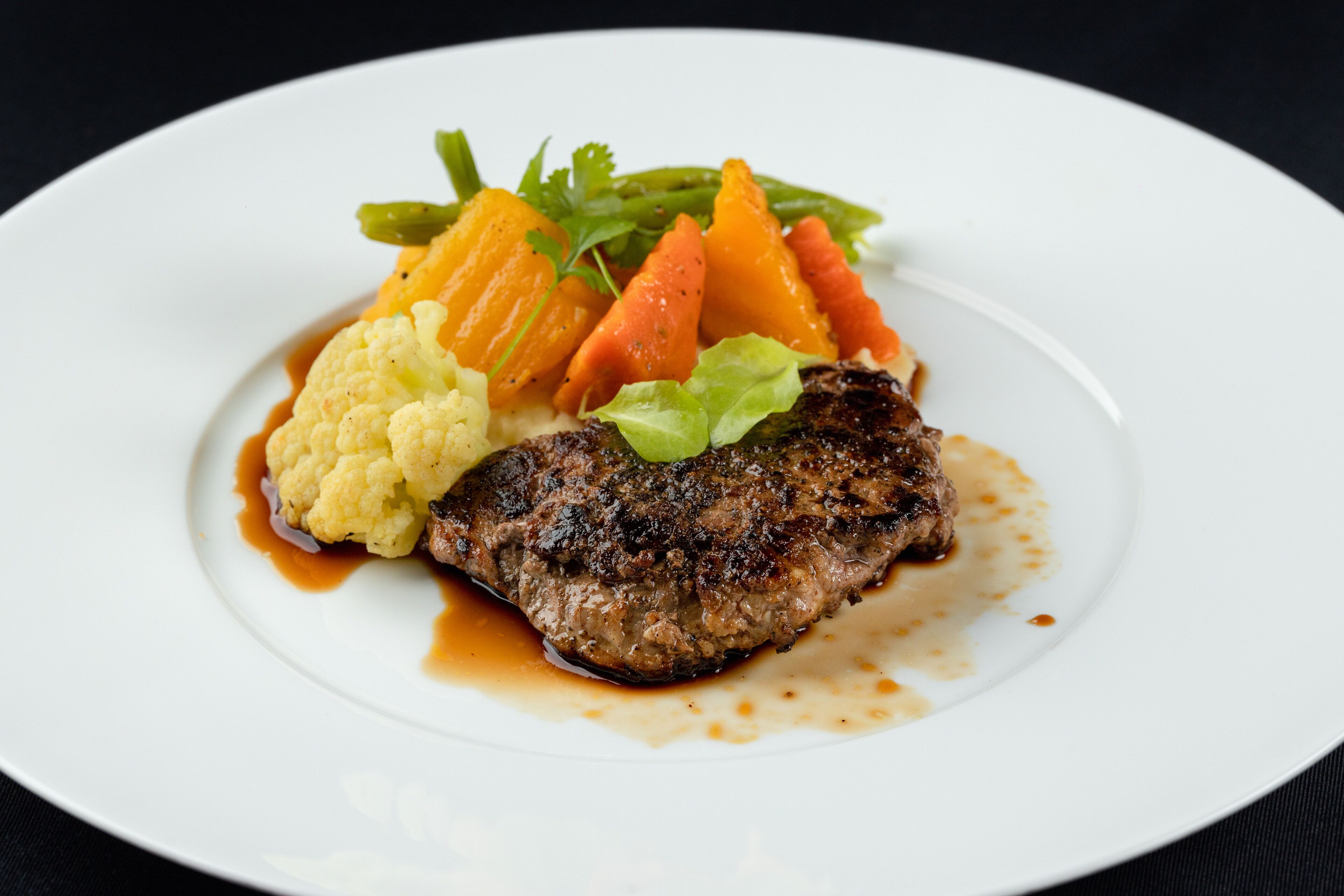 Un plato con un bistec, coliflor, zanahorias y verduras de hoja.