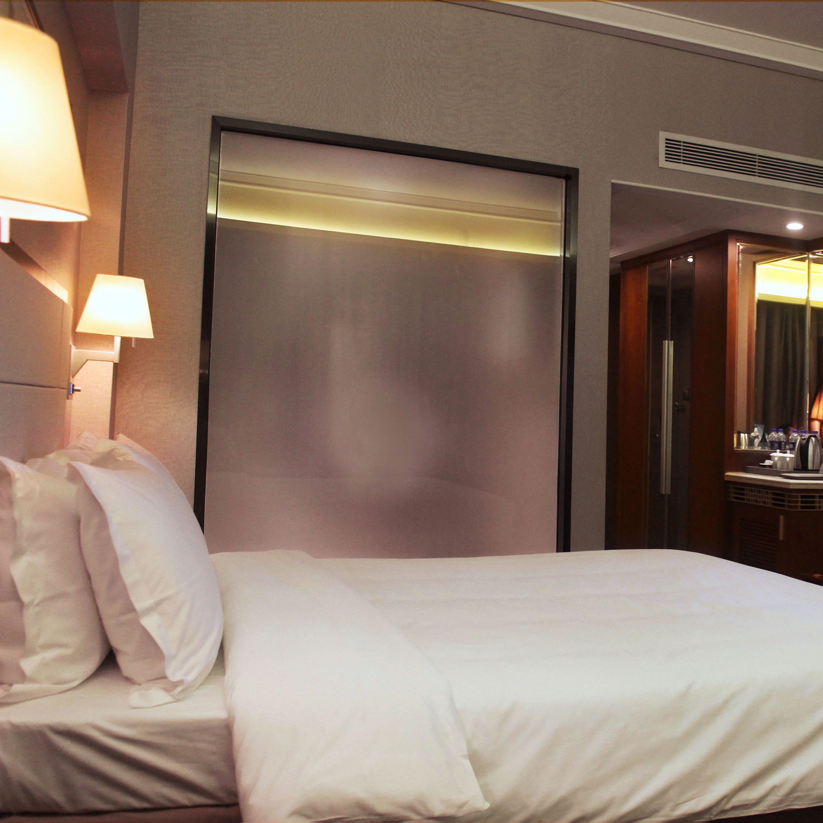 A hotel room with a bed, a nightstand, a lamp, and a mirror.