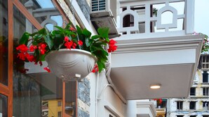 A narrow outdoor corridor with a tiled floor, a staircase on the left, and a balcony with hanging flower pots on the right.