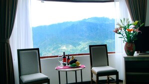 A room with two chairs, a small table with a fruit bowl, wine bottles, and a vase with flowers.
