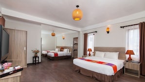 A hotel room with two beds, wooden flooring, a TV, and a small table with a vase of flowers.