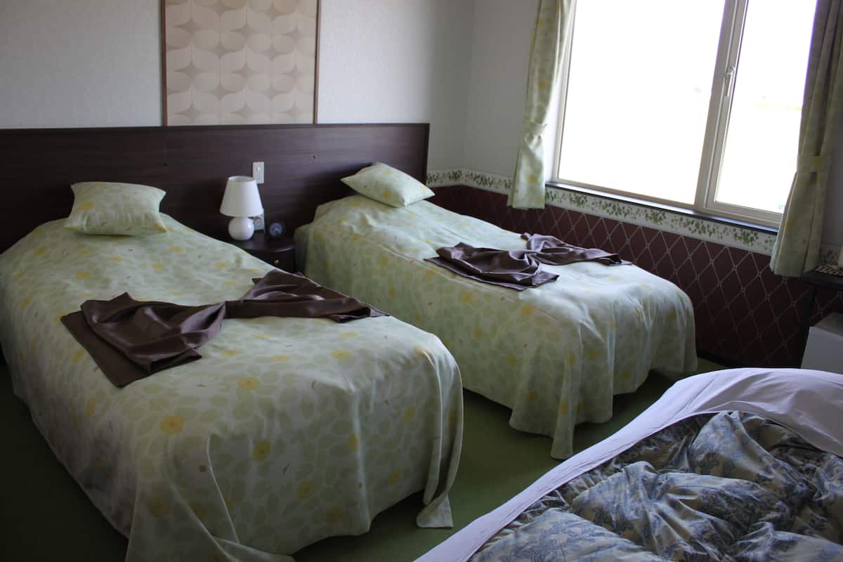 Een hotelkamer met twee enkele bedden, een nachtkastje met een lamp en een raam met gordijnen.