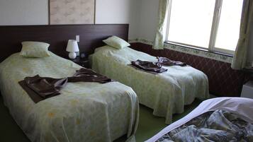 A hotel room with two single beds, a nightstand with a lamp, and a window with curtains.