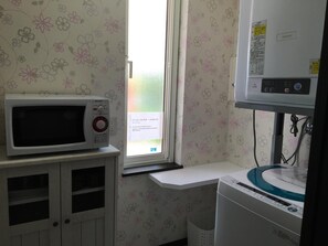 A room with a microwave on a cabinet, a washing machine, and a window with a view. - Petit Hotel Blanc Fleur (Nakafurano)