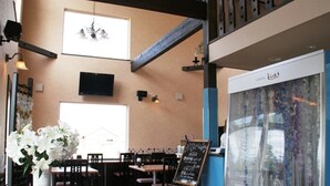 A restaurant interior with wooden tables and chairs, a chalkboard menu, and a large window with natural light. - Petit Hotel Blanc Fleur (Nakafurano)