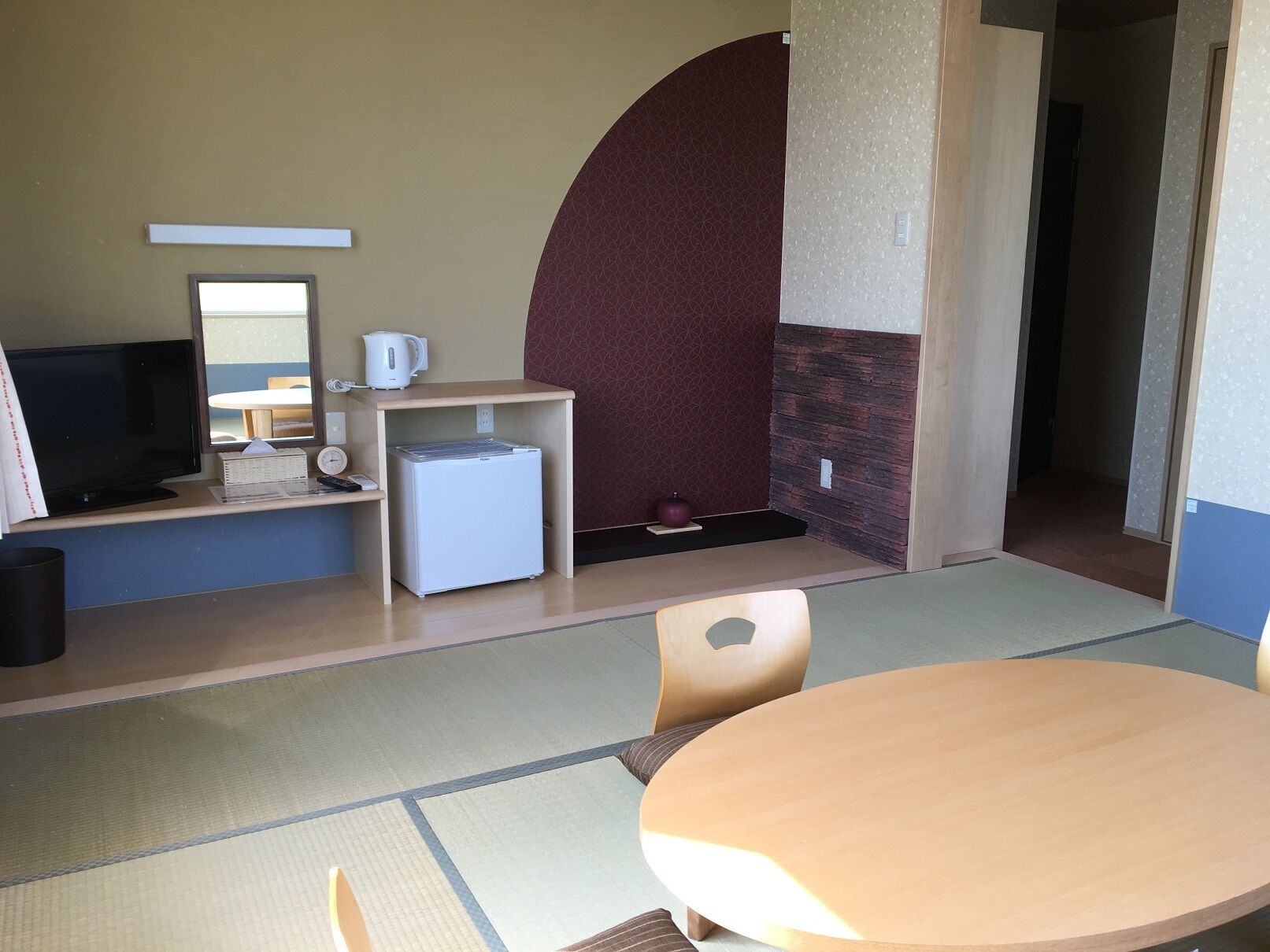 A room with a TV, a small refrigerator, a kettle, a clock, and a round table with chairs.